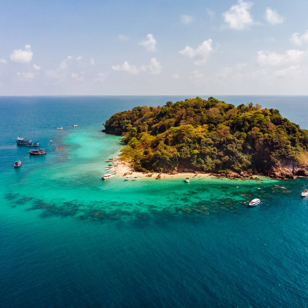 An aerial shot of a small green island in the middle of the ocean with beautiful clouds in the background