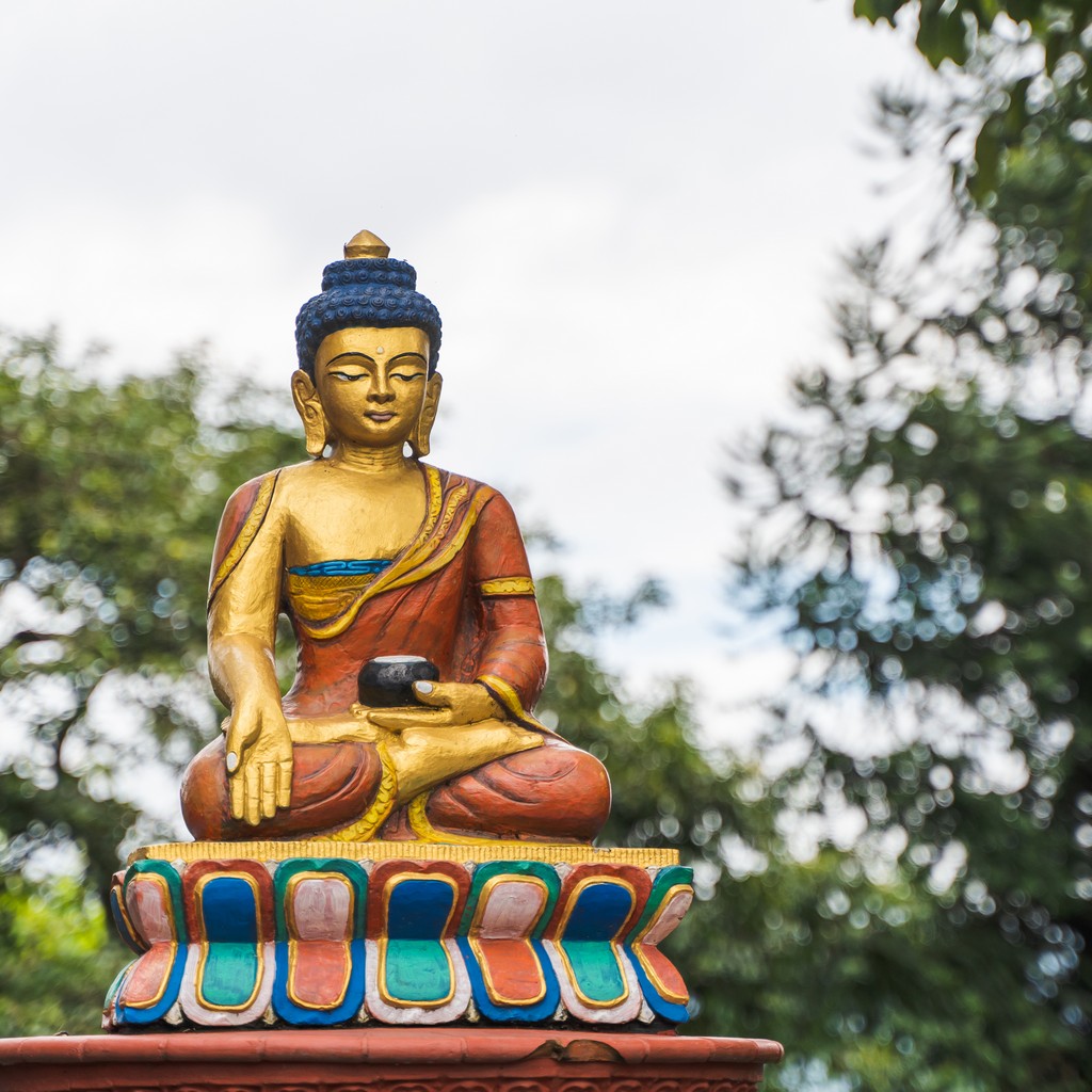 Buddha statue painted in gold with trees and sky on background. Kathmandu city, Nepal.